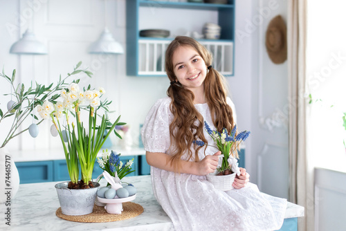 Kid girl sit on kitchen with spring flowers. Happy little girl in dress with ponytails hair holding bouquet flowers. Young Girl and daffodils flowers. Childhood concept. Birthday. Mothers Day.	