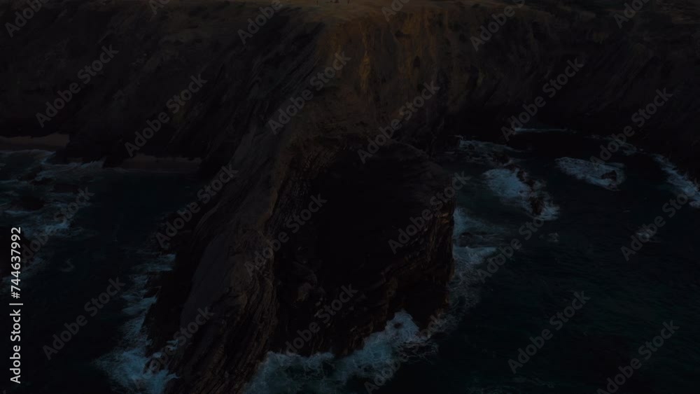 Camera flies over rocky cliffs in dark sunset dusk before night time. Ocean waves crashing on the shore mountain into the white foam. Beauty and power of nature. Camera flies over rocky cliffs in dark sunset dusk before night time. Ocean waves crashing on the shore mountain into the white foam. Beauty and power of nature.