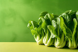 Fresh bok choy on a yellow surface against a green background.
