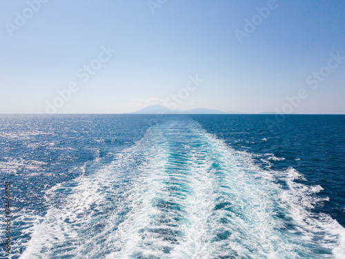 Bright sea water trail behind a cruise ship summer time. Ferry boat leaves a trail in a blue and clear water of Mediterranean Sea leaving Cephalonia island, Greece.