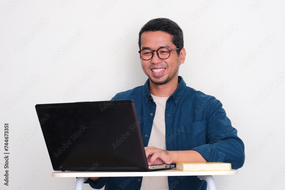 Adult Asian man smiling happy when working using a laptop Adult Asian man smiling happy when working using a laptop