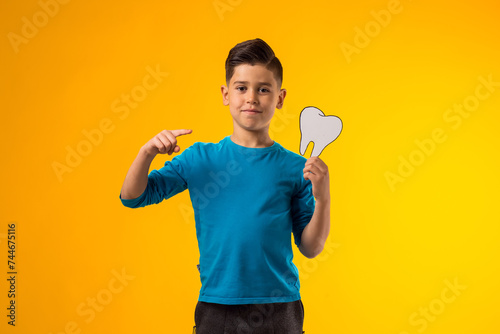 Child boy holding papercraft tooth and pointing finger at it. Dental health concept