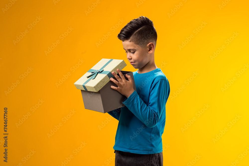 Child boy holding giftbox and looking inside the box over yellow background. Birthday and celebration concept Child boy holding giftbox and looking inside the box over yellow background. Birthday and celebration concept