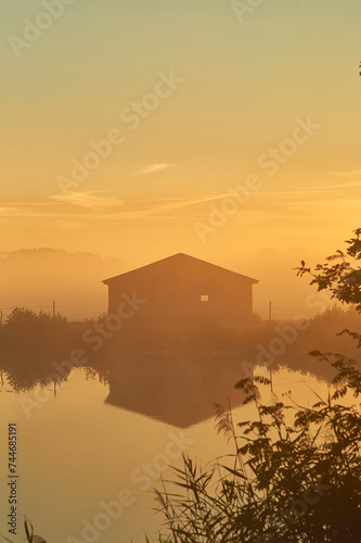 Old barn on lake shore on misty sunrise. High quality photo