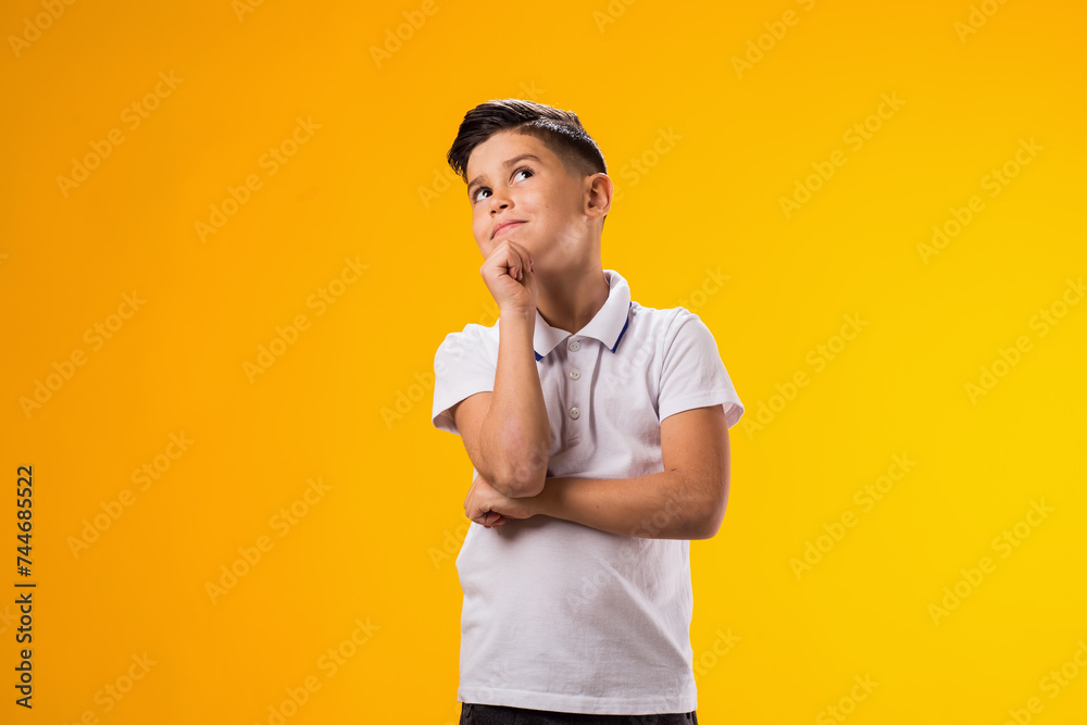 Thoughtful child boy holds chin on yellow background. Dreaming concept Thoughtful child boy holds chin on yellow background. Dreaming concept