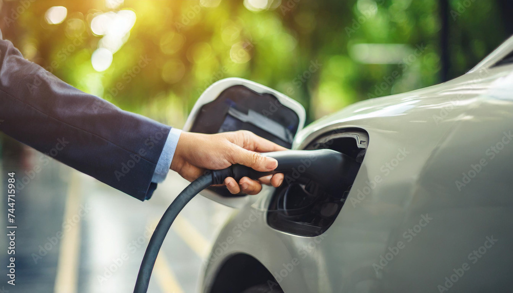 hand plugging in electric car charger, symbolizing eco-consciousness and renewable energy hand plugging in electric car charger, symbolizing eco-consciousness and renewable energy