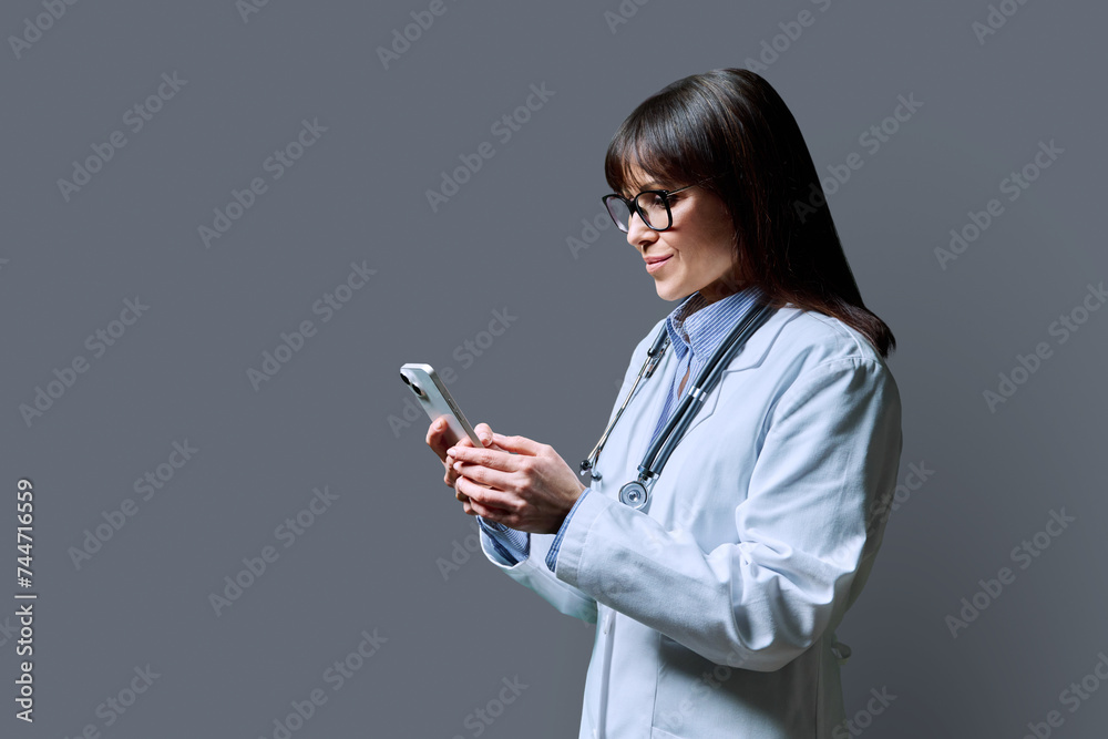 Profile portrait of female doctor using smartphone on gray background Profile portrait of female doctor using smartphone on gray background