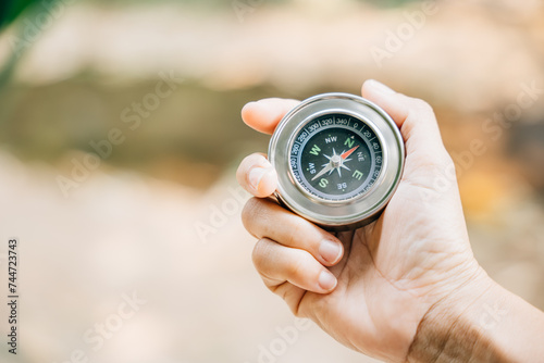 A traveler hand cradles a compass in a park signifying the search for direction and guidance. Amidst nature beauty the compass represents exploration and discovery.