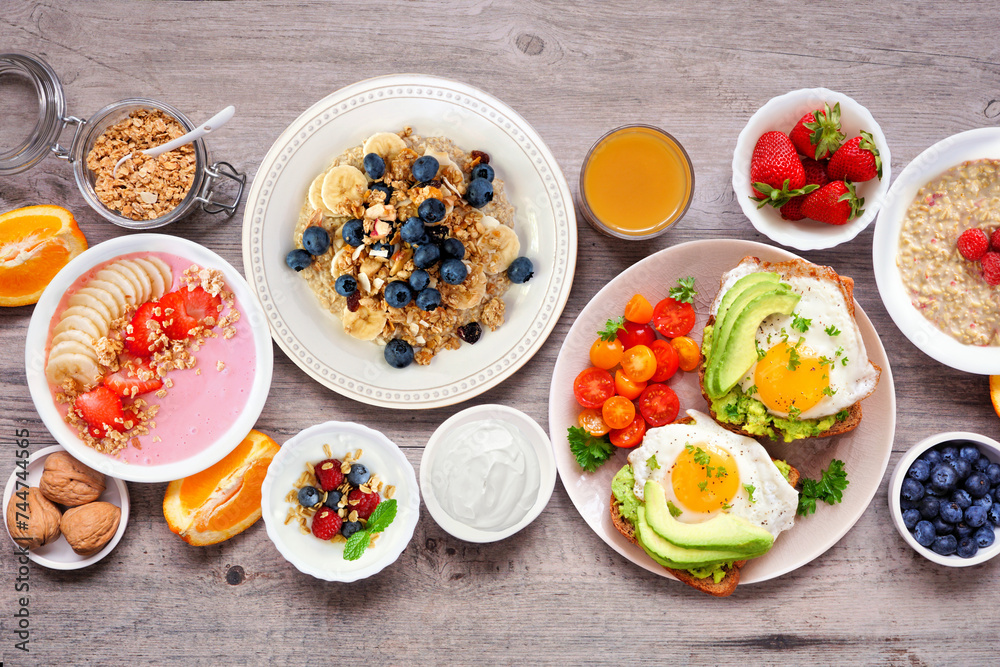 Healthy breakfast or brunch table scene on a wood background. Above view. Avocado toast, smoothie bowls, oats, yogurt and a selection of nutritious foods.