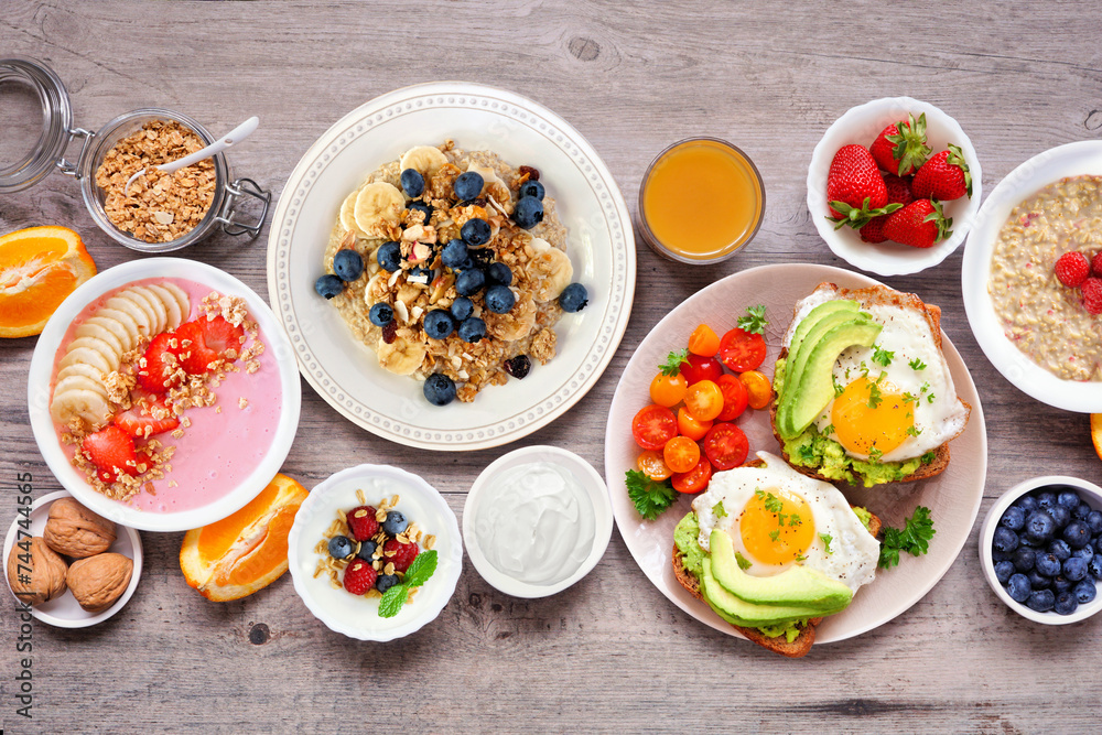 Healthy breakfast or brunch table scene on a wood background. Above view. Avocado toast, smoothie bowls, oats, yogurt and a selection of nutritious foods. Healthy breakfast or brunch table scene on a wood background. Above view. Avocado toast, smoothie bowls, oats, yogurt and a selection of nutritious foods.