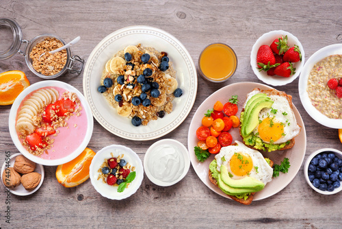 Healthy breakfast or brunch table scene on a wood background. Above view. Avocado toast, smoothie bowls, oats, yogurt and a selection of nutritious foods.