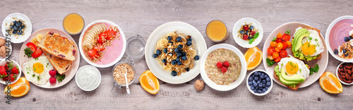 Healthy breakfast or brunch table scene on a wood banner background. Top view. Avocado toast, smoothie bowls, oats, yogurt and a collection of nutritious foods.