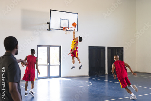 Young African American man jumps for a slam dunk in a basketball game at a gym photo
