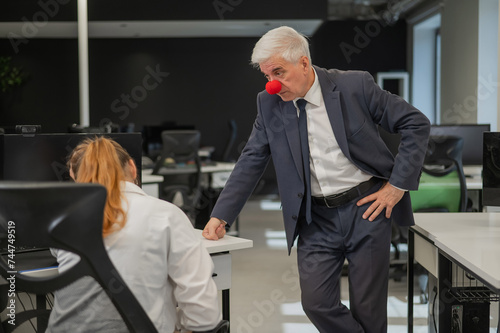 Canvas Print Elderly Caucasian man wearing a clown nose swears at his subordinate in the office