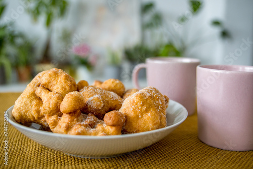 Close-up of a Plate Full of Fallas Fritters with Sugar Sprinkled on Top Next to Two Pink Cups on the Dining Table photo