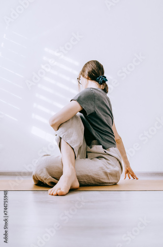 Woman in casual clothes doing seated twist yoga pose on cork mat