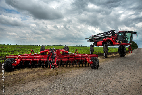 a new harrow cultivator, a self-propelled sprayer stands near a field of gree...