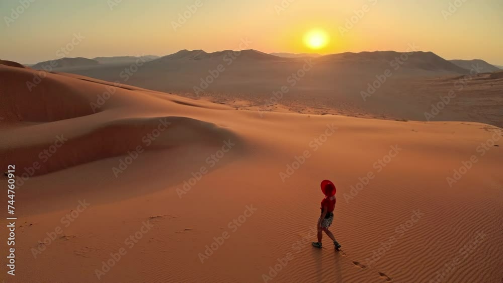 Woman walking in the vastness of the Empty Quarter Rub' al-Khali desert. Red dress in striking contrast to the golden sand at dawn. She seeks adventure and solitude in land of Oman Rub al-Khali desert Woman walking in the vastness of the Empty Quarter Rub' al-Khali desert. Red dress in striking contrast to the golden sand at dawn. She seeks adventure and solitude in land of Oman Rub al-Khali desert