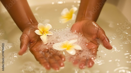 preparing a bath with plumeria flowers for spa treatments. women's hands put flowers in the water © evastar