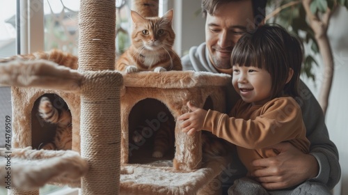 A father and his daughter enjoy a heartwarming moment, playing with their affectionate ginger cats on a cozy cat tree.