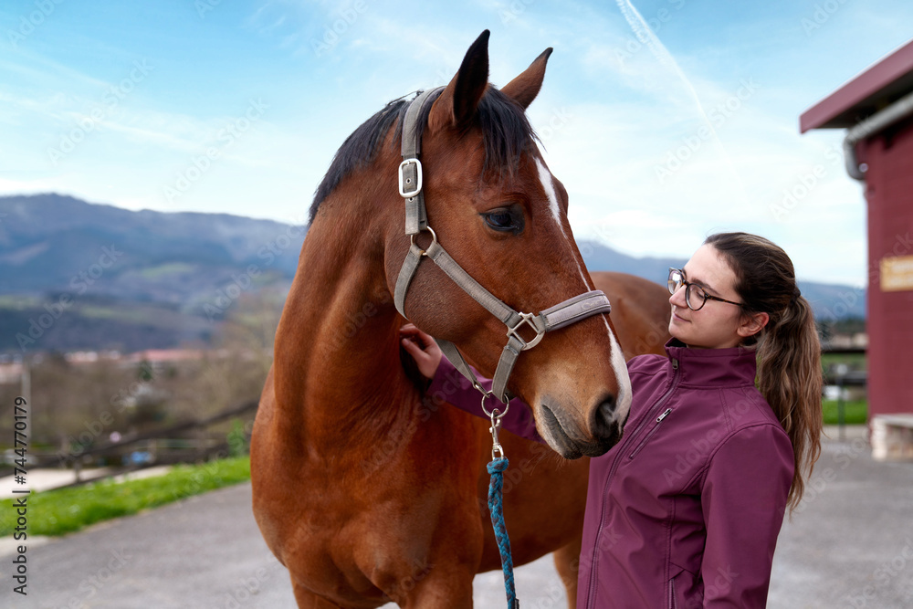 Fototapeta premium A young woman affectionately interacts with a bay horse, with a picturesque mountainous landscape in the background