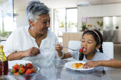 Biracial girl enjoys breakfast of pancakes at home with her grandmother photo