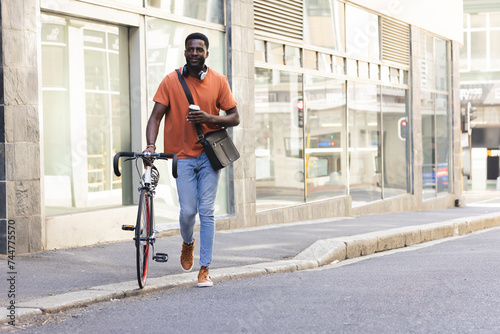 A young African American man walks with his bike outdoors in the city with copy space