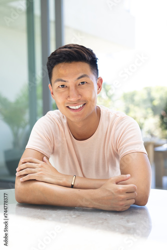 Young Asian man smiles confidently at a bright office setting