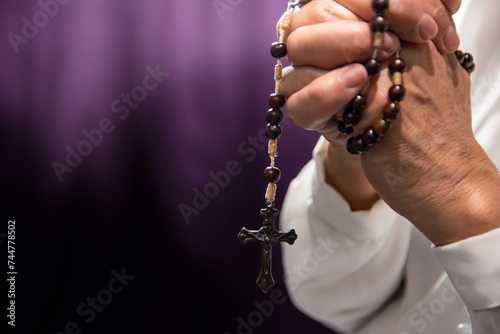 close-up of a rosary in the hand of a mature woman on a purple background