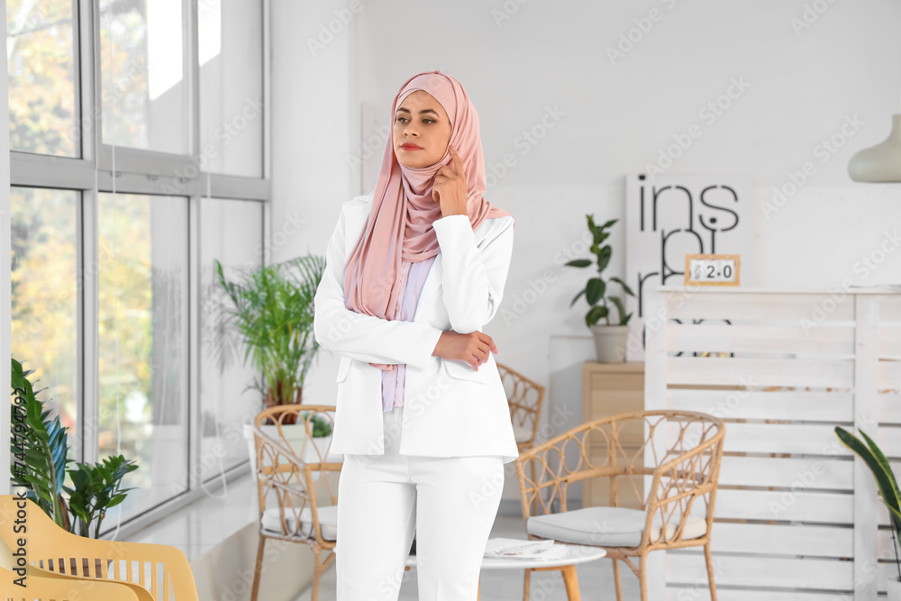 Beautiful young Muslim woman in hijab at office near window Beautiful young Muslim woman in hijab at office near window