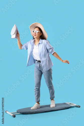 Photography Young Asian woman with iron surfing on ironing board against blue background