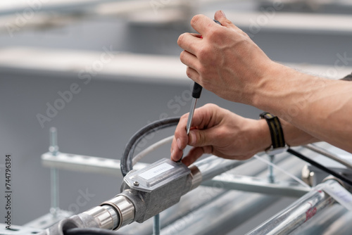A technician's hands carefully adjust a piece of industrial equipment with a screwdriver, precision and focus evident in the meticulous process. Technician Adjusting Industrial Equipment