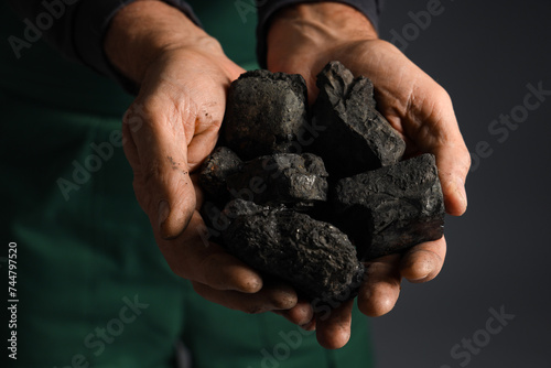 Mature miner man with coal on dark background, closeup