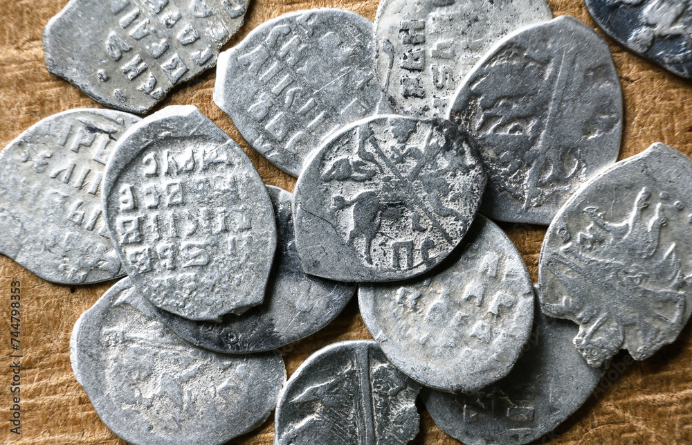 Ancient Russian coins 16th century close-up, pile of silver money of Tsar Ivan IV the Terrible. Top view of metal flakes on vintage background. Concept of old Russia, rare collection - obrazy, fototapety, plakaty 