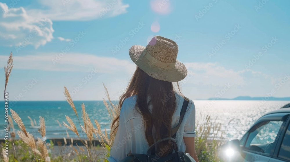 Young woman standing on a cliff and looking at the ocean. She is wearing a hat and a backpack.