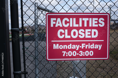 Red and white facilities closed sign hanging on a chain-link fence outside a football stadium.