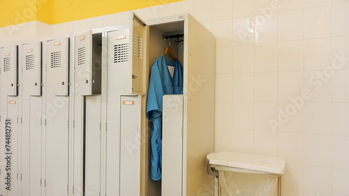 Open metal lockers in the locker room. A nurse's clothes, turquoise smocks and trousers, are hanging on a hanger. Concept of acute shortage of care staff and doctors in hospitals and nursing homes.