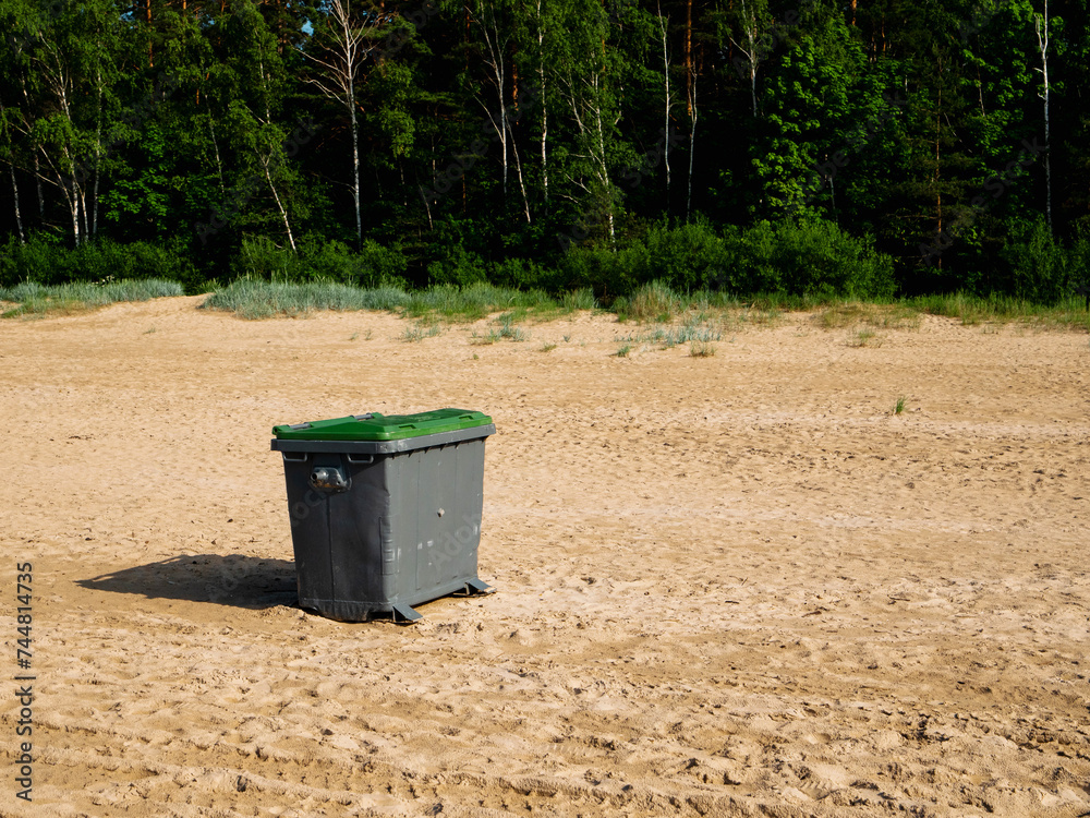 Grey bin with on yellow sandy beach for rubbish collection. Jurmala beach, Latvia. Keeping area clean from dirt concept.