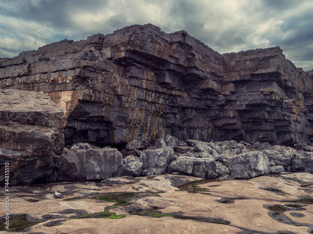 Rough stone coast of Aran island, county Galway, Ireland. Dynamic cloudy sky. Nobody. Coarse rocky shore and cliff.