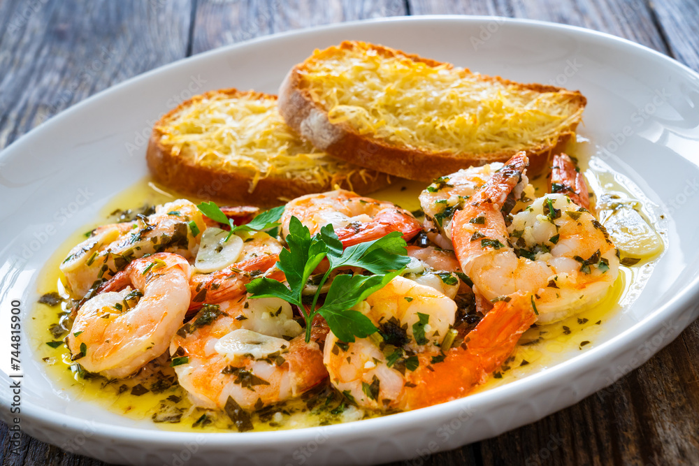 Fried shrimps with garlic and parsley in olive oil and toasted bread with parmesan cheese on wooden table Fried shrimps with garlic and parsley in olive oil and toasted bread with parmesan cheese on wooden table