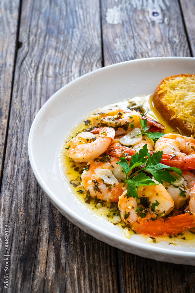 Fried shrimps with garlic and parsley in olive oil and toasted bread with parmesan cheese on wooden table Fried shrimps with garlic and parsley in olive oil and toasted bread with parmesan cheese on wooden table