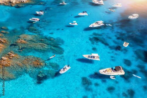Aerial view of luxury yachts and boats on blue sea on summer sunny day. Travel in Sardinia, Italy. Top drone view of speed boats, yachts, sea bay, rocky coast, transparent water. Seascape. Travel