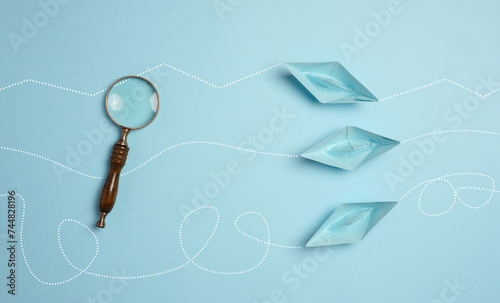 Photography Blue paper boats and a magnifying glass, viewed from above