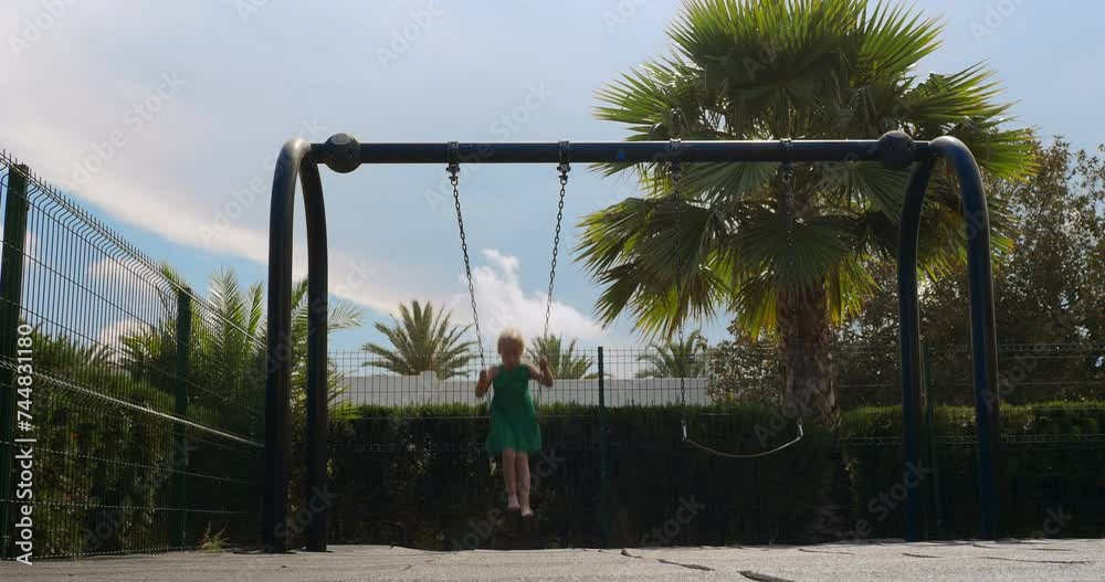 Child swinging on a playground swing set with trees in the background Child swinging on a playground swing set with trees in the background