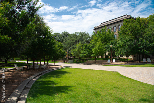 Brick walkway and outdoor seating with adirondack chairs under canopy tree shade summertime at grassy Texas college campus, ample green space, historic buildings, education, landscaping concept photo