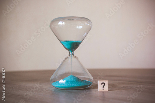 hourglass with a question mark written on a wooden cube. Time management concept. Word "?" next to an hourglass. the concept of interrogation. concept of an enigma