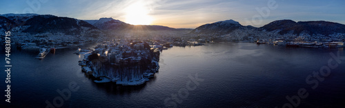 Early morning winter drone aerial panorama of Bergen city in Norway. Sun rising up behind a city cramped between mountains. Epic view of Bergen in the morning.