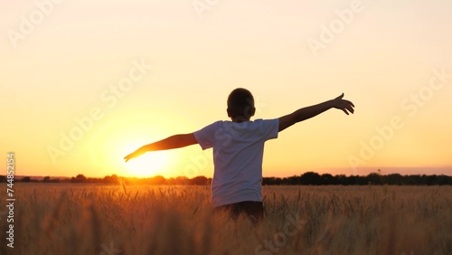 Overjoyed male teenager speed running on wheat field picturesque sunset sunrise bright sun light sky back view. Teen boy movement with raised hands enjoy freedom happy childhood at countryside meadow
