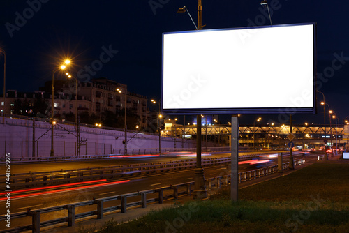 Horizontal billboard near an illuminated highway in the city at night. Mock-up.