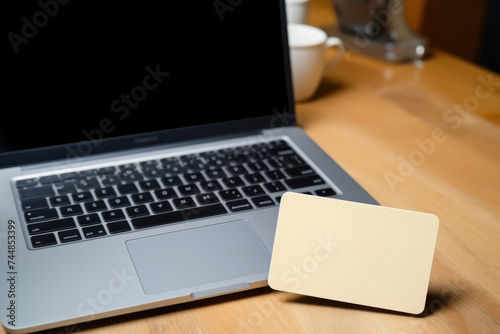 An open laptop with a yellow note card, set on a wooden desk beside a coffee cup, suggesting productivity or planning. Laptop and Coffee with Blank Yellow Card